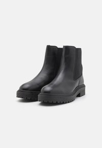 Botas de tobillo de cuero negro con paneles elásticos en los laterales, puntera redondeada y suela de goma texturizada y gruesa. Acabado suave con detalles de costura.