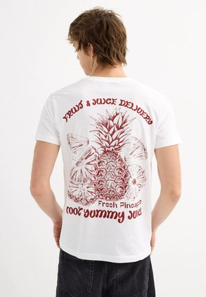 Camiseta blanca con un gráfico rojo de una piña y otras frutas, con el texto "Entrega de Frutas y Jugos" y "Piña Fresca" impreso arriba.
