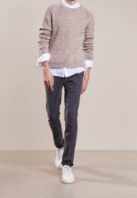 Maglione lavorato a maglia color beige chiaro con una finitura texturizzata, abbinato a pantaloni grigi e sneakers bianche. Il maglione presenta orli e polsini a costine.