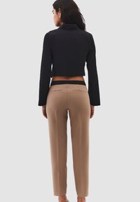 Ingekorte zwarte jas met lange mouwen en gestructureerde kraag, gecombineerd met slim-fit beige broeken met twee achterzakken en op maat gemaakte naden.