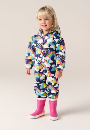 Tuta impermeabile colorata con sfondo blu navy decorata con arcobaleni, ombrelli e nuvole. Completata da stivali di gomma rosa con suole bianche.