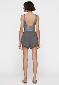 Bañador gris con estampado y espalda baja, pantalones cortos grises con dobladillo curvado y bolsillo lateral, combinados con chanclas grises.