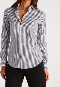 Gestreiftes Hemd in Marineblau und Weiß aus Baumwolle, mit einem spitzen Kragen und einem kleinen Logo auf der Brust. Lange Ärmel mit Manschettendetails.