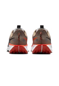 Las zapatillas deportivas cuentan con una parte superior de malla beige con detalles en negro y naranja, un tacón medio y una suela texturizada en blanco y rojo.