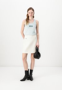 Haut sans manches bleu clair avec "BOSS" brodé en fil sombre, associé à une mini-jupe blanche texturée et des bottines noires.