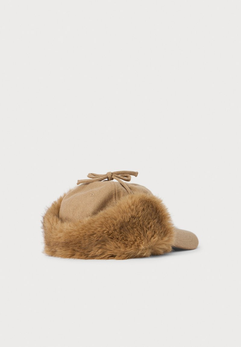 Beige baseball cap with a brown faux fur trim lining the sides and a tied bow detail on top, displayed on a white background.