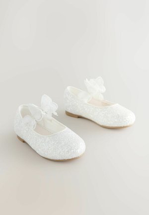 Fehér csillogó balettcipő lekerekített orral, díszítő fehér virágmotívummal és texturált, csillogó felülettel.