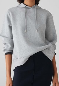 Sweat à capuche gris clair en tissu doux, doté d'une capuche à cordon et de poignets côtelés, conçu avec une coupe décontractée et un ourlet légèrement raccourci.