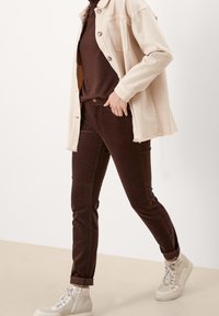 Chaqueta de mezclilla beige, suéter ajustado marrón y pantalones de pana marrón oscuro, combinados con zapatillas altas beige. Diseño simple con bordes deshilachados.