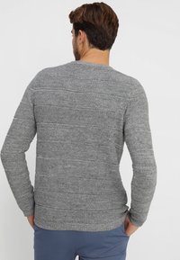 Pull gris en tricot avec des rayures horizontales texturées, manches longues et col rond. Le tissu a une apparence douce et confortable.