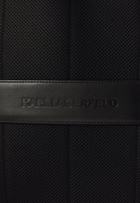 Tissu en mesh noir avec des accents en cuir texturé. Présente le logo "KARL LAGERFELD" embossé sur une bande de cuir horizontale.