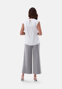Camicia bianca con scollatura plissettata e dettagli a chiave sul retro, abbinata a pantaloni larghi grigi a vita alta. Tessuto liscio e leggero.