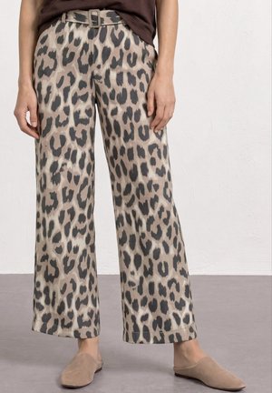 Beige viddebenede bukser med sort leopardprint, bælte i taljen, båret med lysebrune slip-on sko og en mørk top.
