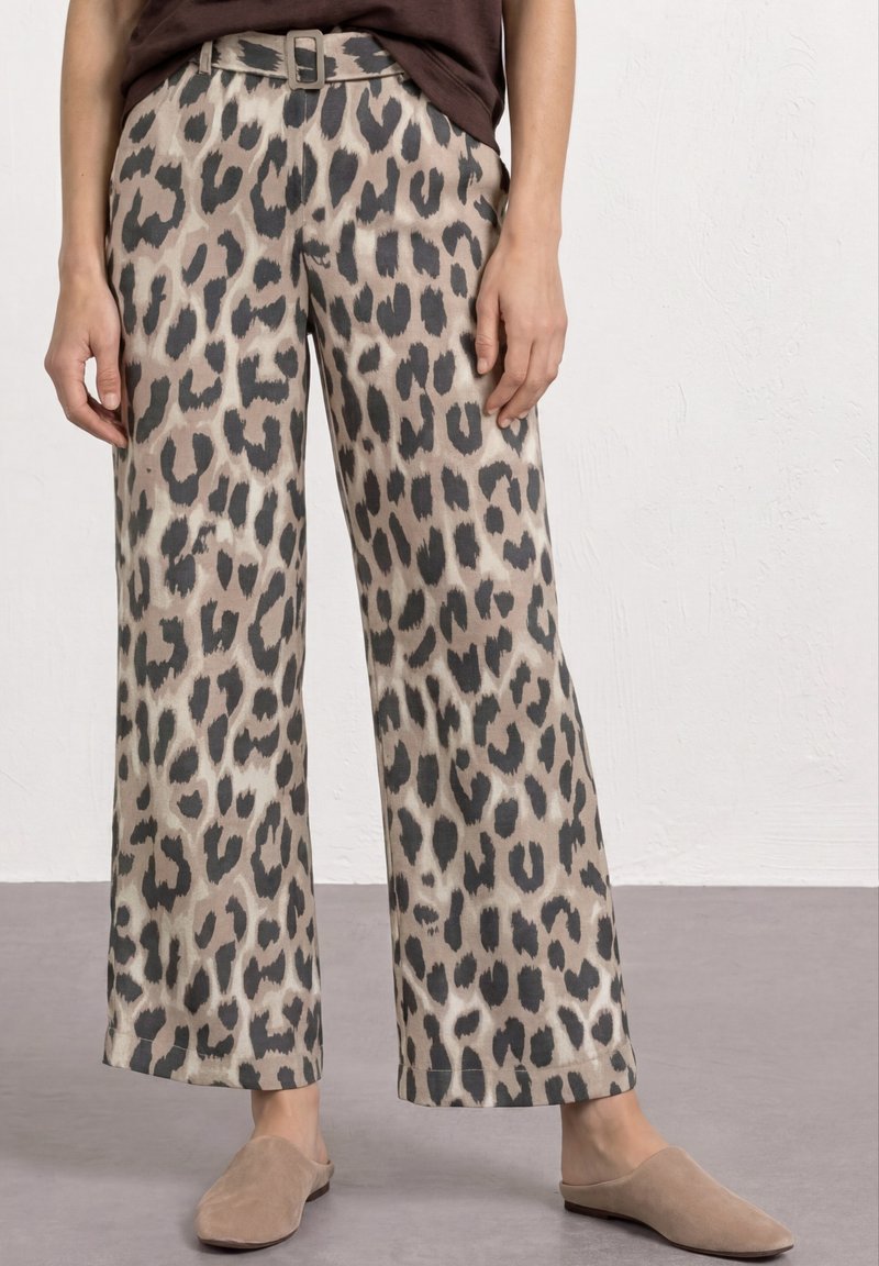 Beige viddebenede bukser med sort leopardprint, bælte i taljen, båret med lysebrune slip-on sko og en mørk top.