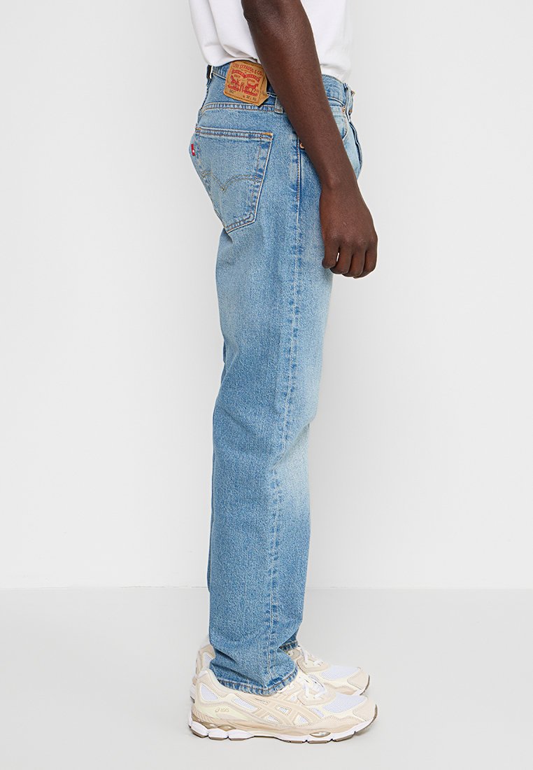 Hellblaue Jeans aus Denim mit geradem Bein und Gesäßtaschen, versehen mit einem braunen Lederpatch am Bund und subtilen Verfärbungen.