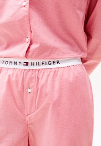 Chemise à carreaux rouge et blanc associée à un short à carreaux rougess. Le short présente une taille élastique avec la marquage "TOMMY HILFIGER".