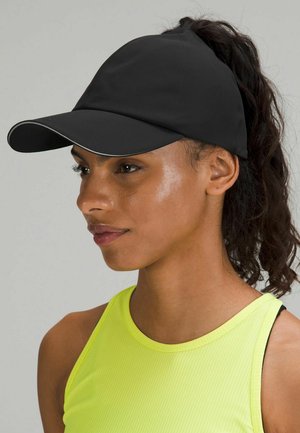 Cappellino sportivo nero con visiera curva e rifiniture riflettenti, progettato per ospitare un ponytail. Indossato con una maglietta senza maniche di un brillante colore giallo.