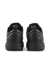 Zapatillas negras con parte superior de cuero suave, forma redondeada, collar acolchado y suela de goma. Etiquetas visibles en el interior del calzado.