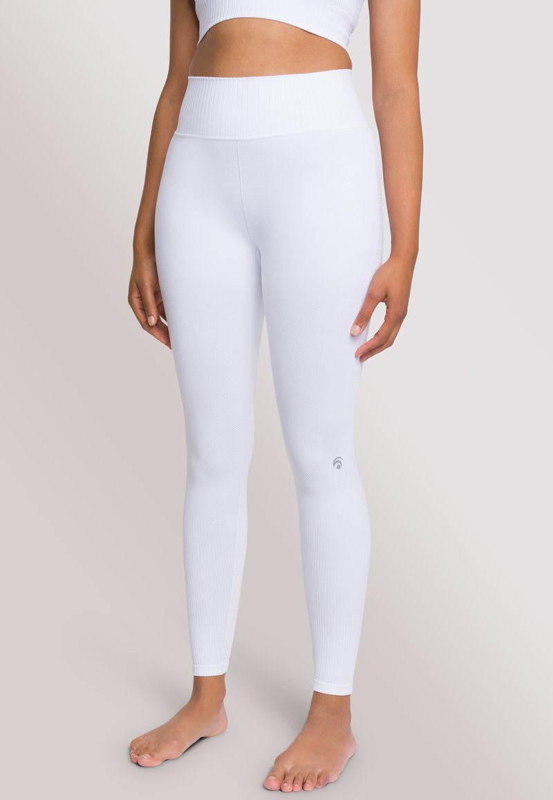 Leggings bianchi a coste con vita alta, caratterizzati da un accento logo sulla parte inferiore della gamba. Texture liscia, design aderente e senza cuciture visibili.