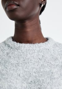 Pull gris texturé avec un col rond et un matériau doux et duveteux. Vue en gros plan du col et du cou, sans motifs ni éléments métalliques visibles.