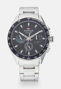 Montre en acier inoxydable argenté avec un cadran noir, une lunette tachymétrique et trois sous-cadrans. Comprend des index lumineux et un affichage de la date.
