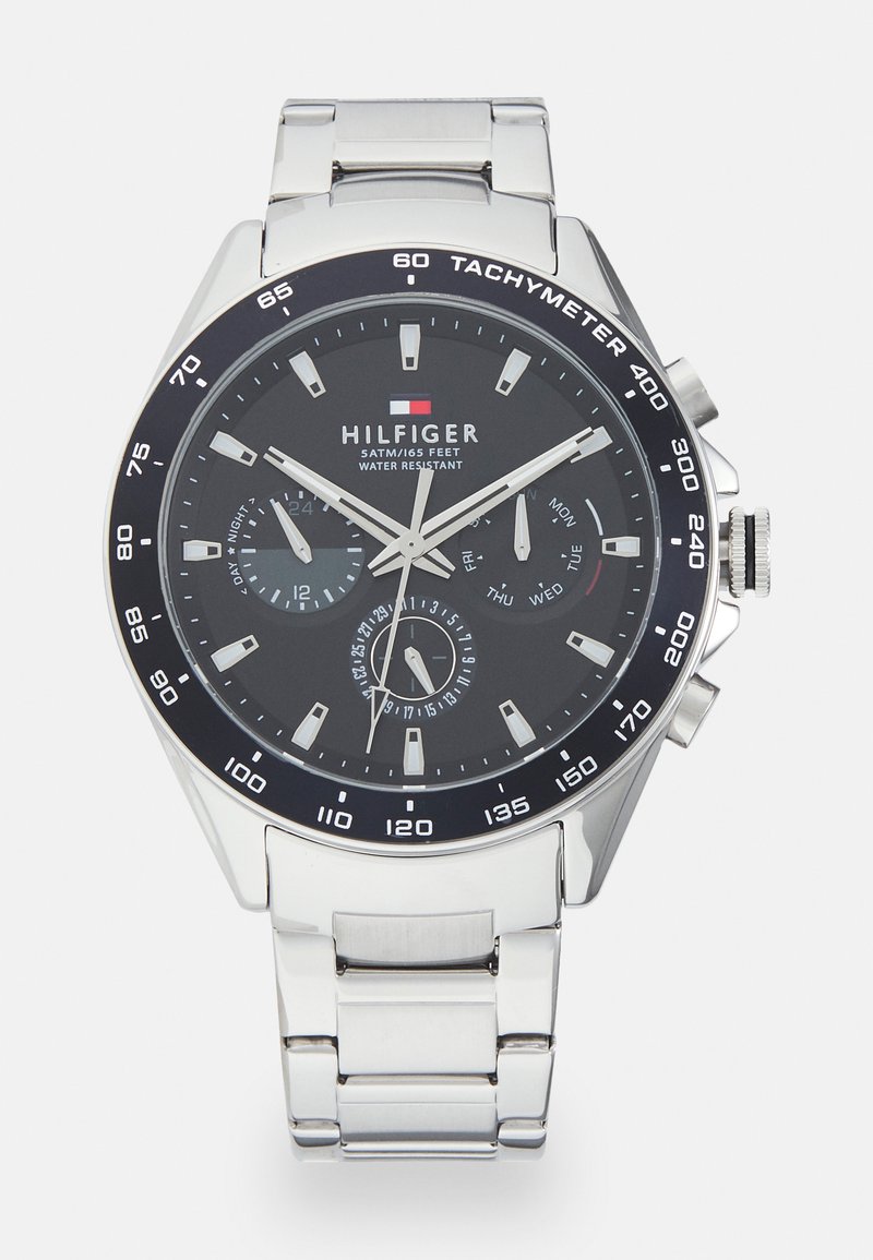 Montre en acier inoxydable argenté avec un cadran noir, une lunette tachymétrique et trois sous-cadrans. Comprend des index lumineux et un affichage de la date.