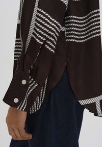 Camicia a righe bianco e nero con maniche lunghe, polsini con bottoni e una texture liscia; presenta spacchi laterali per una vestibilità rilassata.