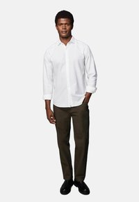 Weißes Hemd mit langen Ärmeln, kombiniert mit dunkelolivgrünen Hosen und schwarzen Stiefeln. Einfaches Design, taillierte Silhouette und ohne Muster.
