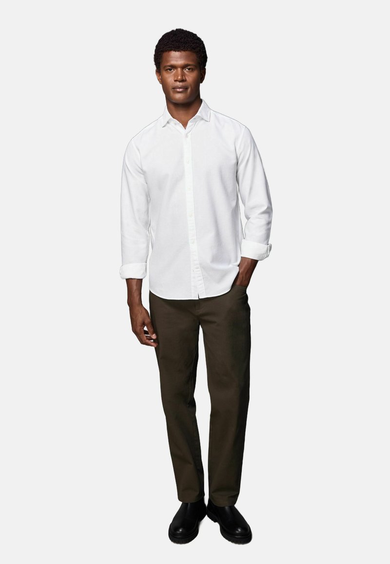 Weißes Hemd mit langen Ärmeln, kombiniert mit dunkelolivgrünen Hosen und schwarzen Stiefeln. Einfaches Design, taillierte Silhouette und ohne Muster.