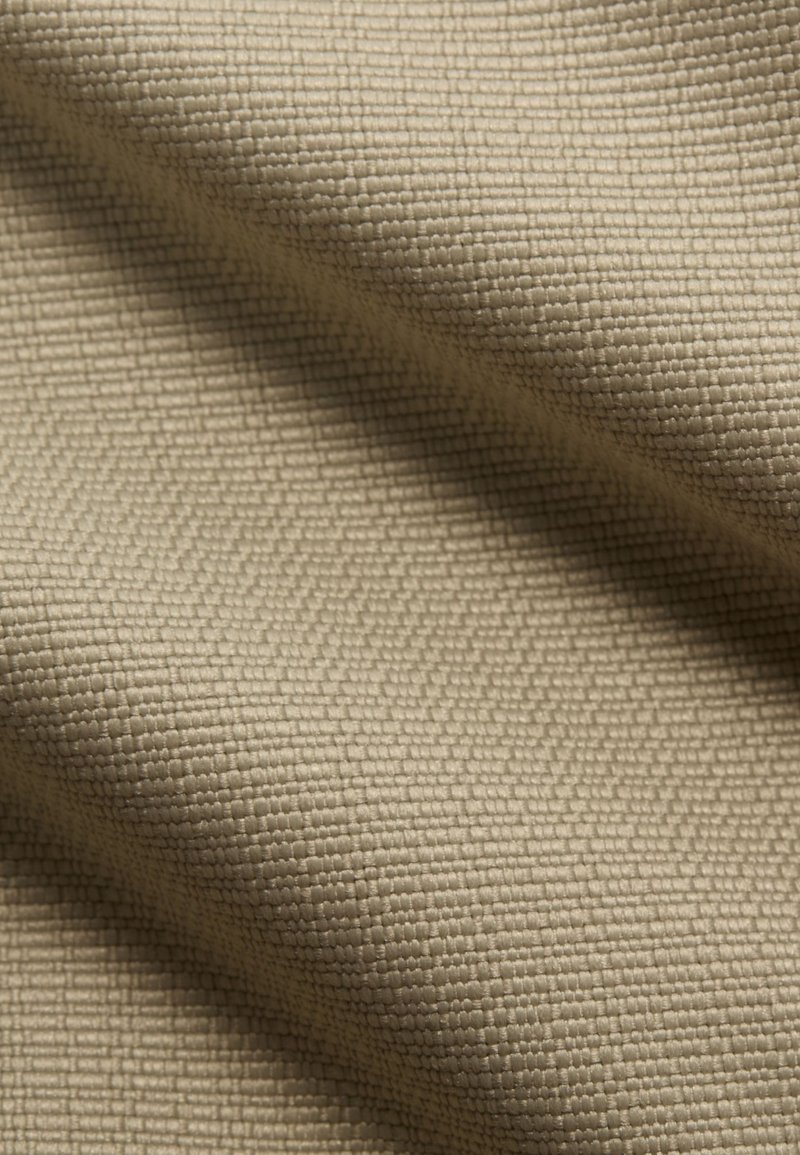 Beige texturerat tyg som visar ett vävt mönster med ett rutliknande utseende, vilket betonar dess mjuka, hållbara struktur och neutrala färg.