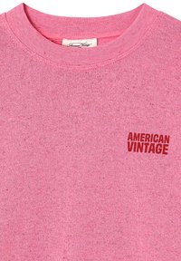 Pull rose tricoté à col rond avec un logo texte "American Vintage" rouge sur la poitrine gauche et une étiquette de marque blanche à l'intérieur du col.