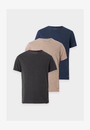 Homme portant un t-shirt gris foncé, un short gris clair, des chaussettes blanches et des baskets blanches, debout devant un fond blanc uni.