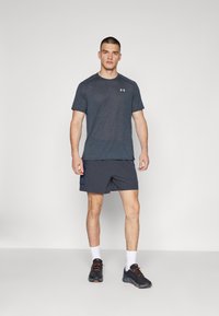 Träningskläder för män med en marinblå fukttransporterande T-shirt och matchande shorts. Skorna är svarta med orange accenter.
