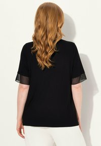 T-shirt noir avec des manches courtes en maille, coupe ample et ourlet arrondi. Texture douce, détails minimaux sur le tissu.