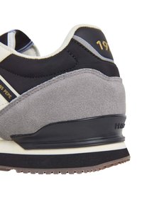Sneaker with a black textile upper, gray suede accents, and a white midsole. Features gold logo detail and patterned rubber outsole.