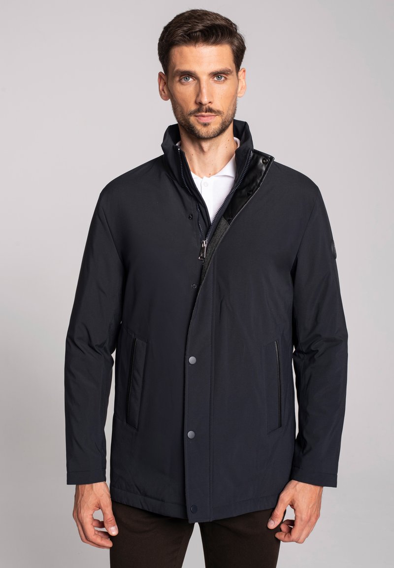 Granatowa kurtka zapinana na zamek z wysokim kołnierzem, z zatrzaskami i bocznymi kieszeniami. Wykonana z gładkiego, lekkiego materiału.
