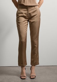 Braune, maßgeschneiderte Hosen mit glatter Oberfläche, gerade geschnitten und mit umgeschlagenen Säumen, kombiniert mit schwarzen Riemchensandalen.
