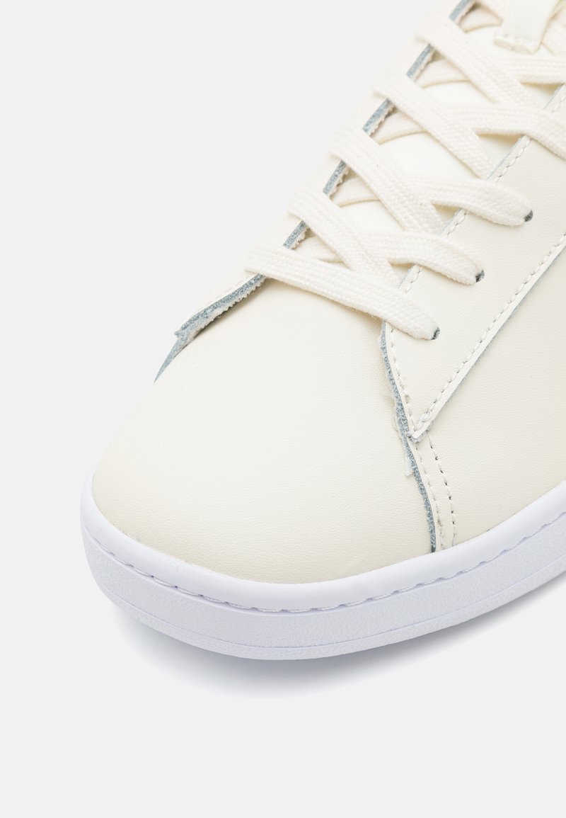 Białe skórzane sneakersy z zaokrąglonym noskiem, teksturowanym panelem bocznym i płaskimi sznurowadłami; mają białą gumową podeszwę i jasnoniebieskie detale przeszyć.