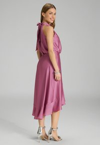 Gaun satin merah jambu dengan leher terikat, pinggang elastik, dan hem berkibar. Dipadukan dengan sandal hak tinggi berwarna perak.