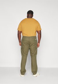 Olijfgroene cargobroek met zijzakken, gecombineerd met een mosterdgele t-shirt, gedragen met witte sneakers. Zicht van achter.