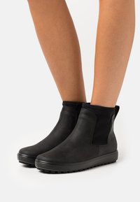 Bocanci negri până la gleznă cu un finisaj din piele netedă, panouri laterale elastice, talpă din cauciuc și un design minimalist. Potriviți pentru îmbrăcăminte casual.