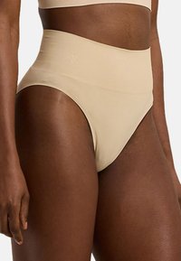 Högmidjade beige underkläder i mjukt, stretchigt tyg med minimala sömmar, med en logodetalj på midjebandet och en sömlös design.