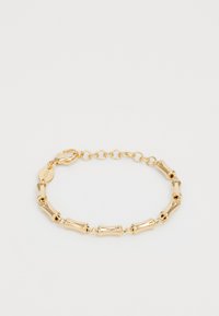 Bracelet en or avec des maillons tubulaires courbés et un fermoir à chaîne ajustable sur un fond clair.
