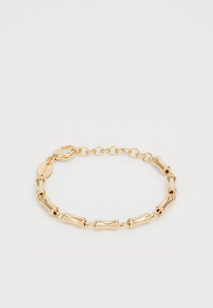 Goldene Armbanduhr mit gebogenen röhrenförmigen Gliedern und verstellbarem Kettenverschluss auf einem schlichten, hellen Hintergrund.