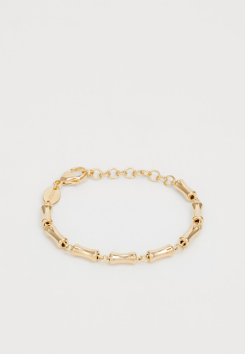 Bracelet en or avec des maillons tubulaires courbés et un fermoir à chaîne ajustable sur un fond clair.
