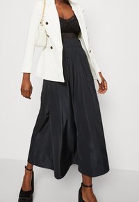 Blazer bianco doppiopetto, top in pizzo nero, culotte in satin nero a vita alta e tacchi alti neri con cinturini alla caviglia.