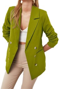 Zielona dwurzędowa marynarka z wyciętymi klapami, wszytymi poduszkami na ramionach oraz dwoma przednimi kieszeniami. Dopasowany krój z srebrnymi guzikami i podwiniętymi rękawami.