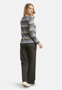 Long-sleeve, multicolored sweater with a zigzag pattern in blue, gray, and cream, paired with dark gray wide-leg pants and white sneakers.