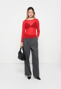 Rød blonde langermet topp over en tonalt bralette, kombinert med høyt liv grå bukser. Akkompagnert av en svart vevd håndveske og spisse sko.