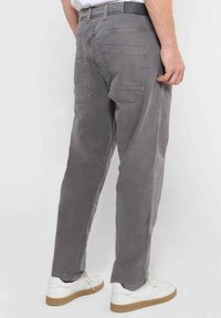 Grijze katoenen broek met een ontspannen pasvorm, voorzien van twee achterzakken en een gestructureerde afwerking. Gepaard met witte sneakers.